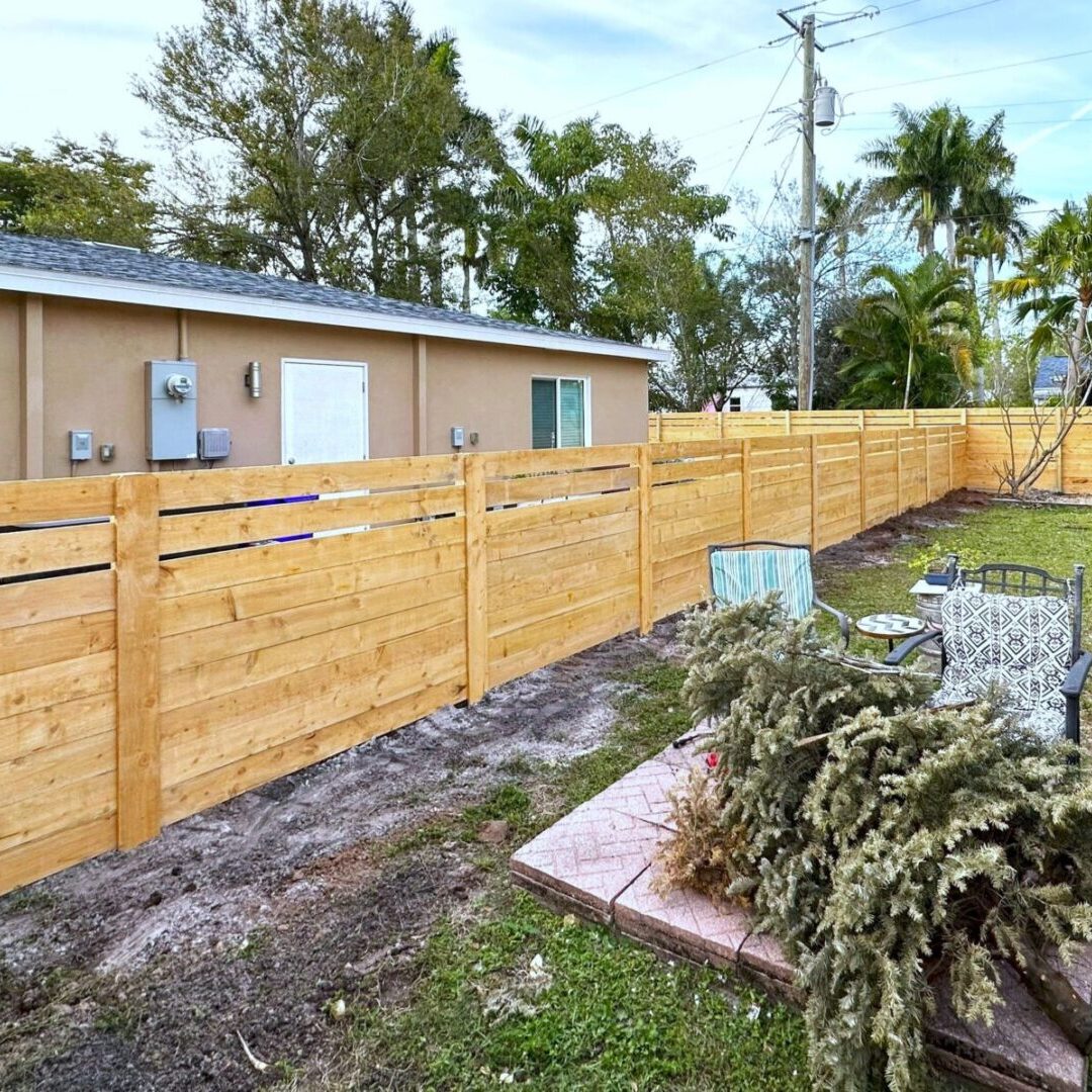 A wooden fence is shown with a house in the background.