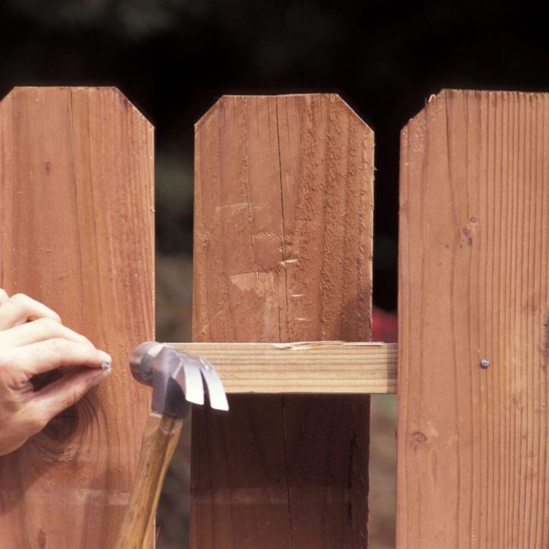 A person painting the side of a wooden fence.