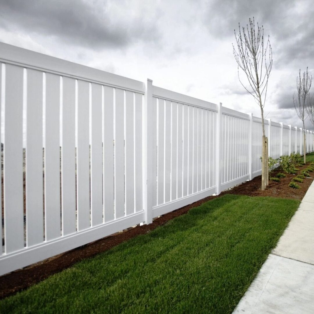 A white fence with grass growing on the side.